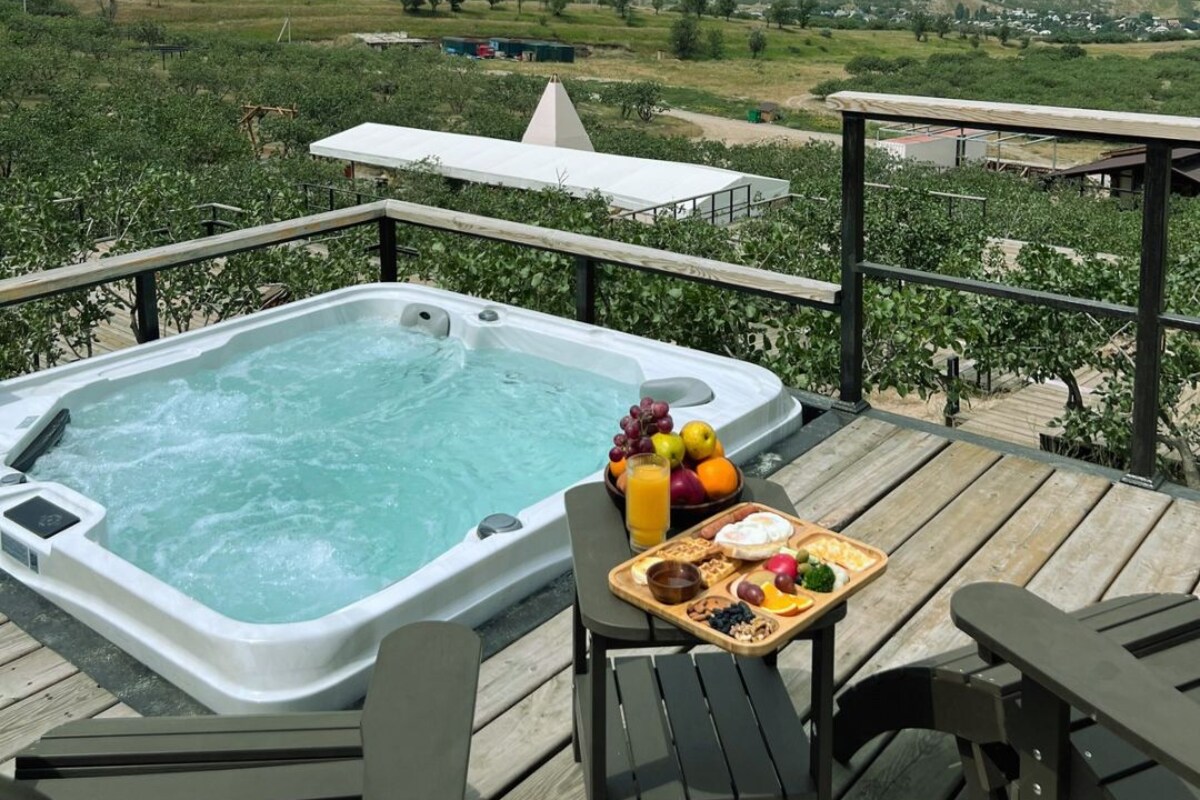 Un bain à remous sur une terrasse, avec une table et des chaises, donnant sur un vignoble et des collines.