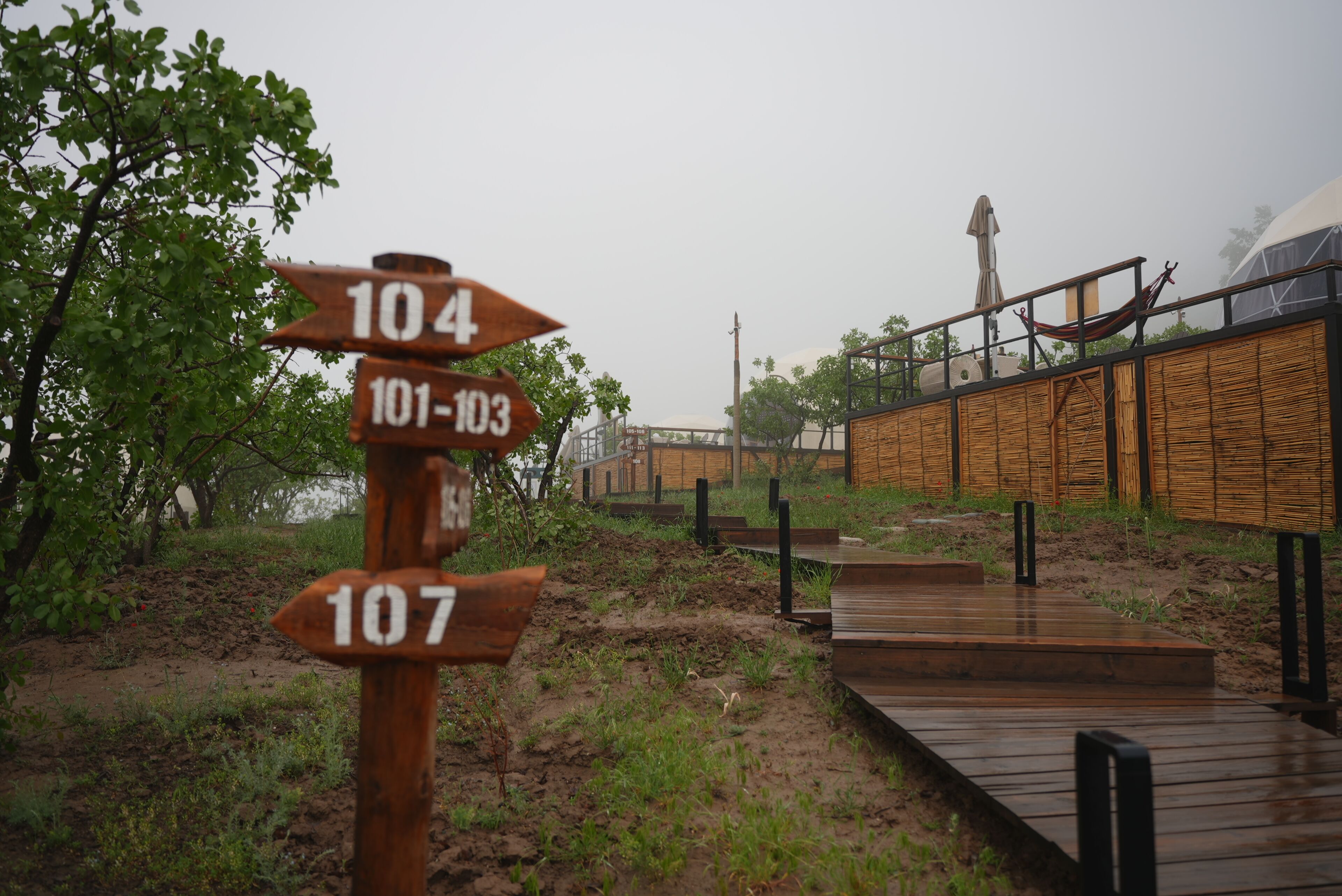 A wooden signpost with directional arrows and numbers, a wooden deck, and a bamboo fence in a natural setting.