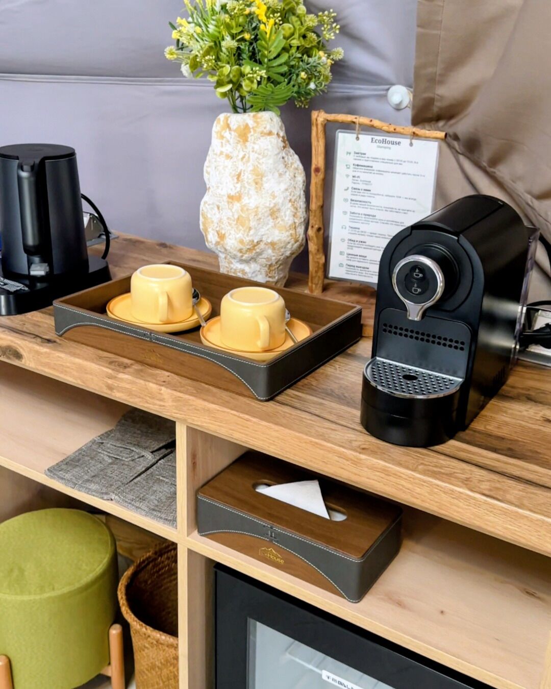 A wooden desk with a coffee maker, two yellow cups, a vase with flowers, and a menu sign.