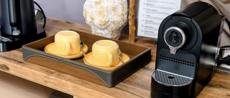 A wooden desk with a coffee maker, two yellow cups, a vase with flowers, and a menu sign.