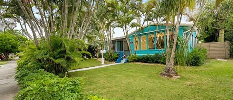 A house with a blue exterior, surrounded by lush greenery and palm trees.