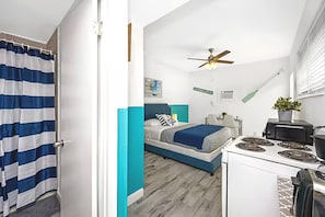 A compact bedroom with a bed, a ceiling fan, and a kitchenette.