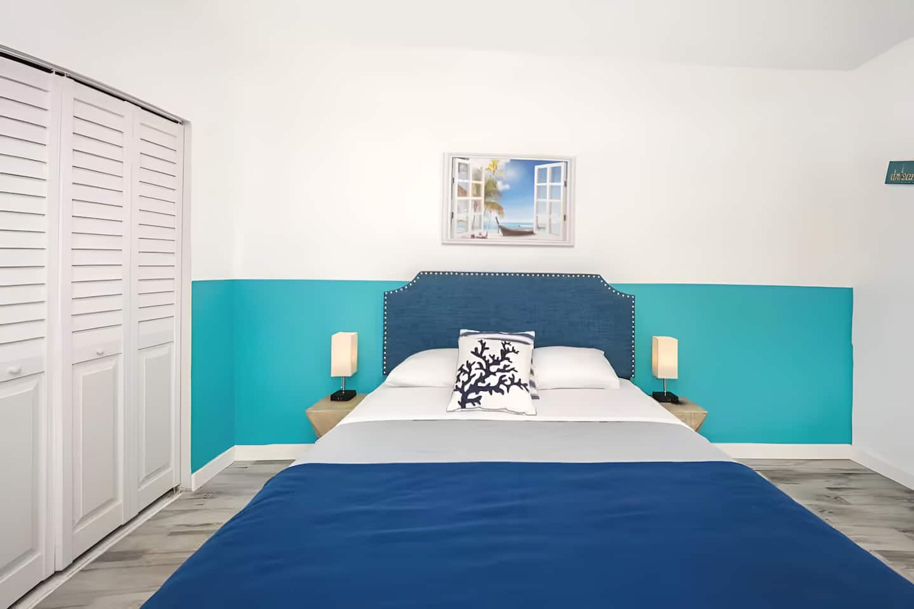Une chambre à coucher comprenant un lit, deux tables de chevet avec des lampes, une fenêtre donnant sur la mer et une porte à mécanisme coulissant.