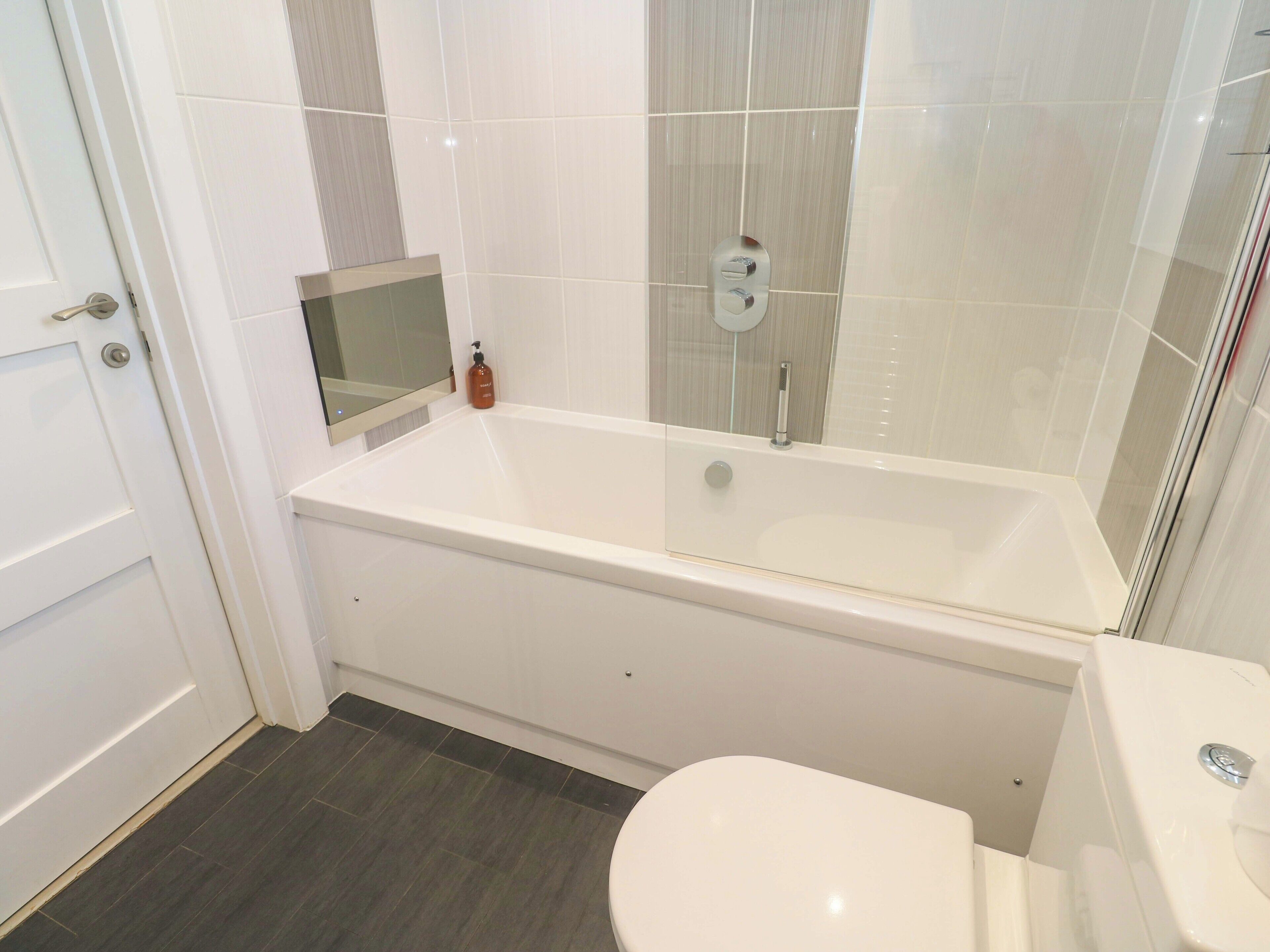 A modern bathroom with a white bathtub, a toilet, and a glass shower enclosure.