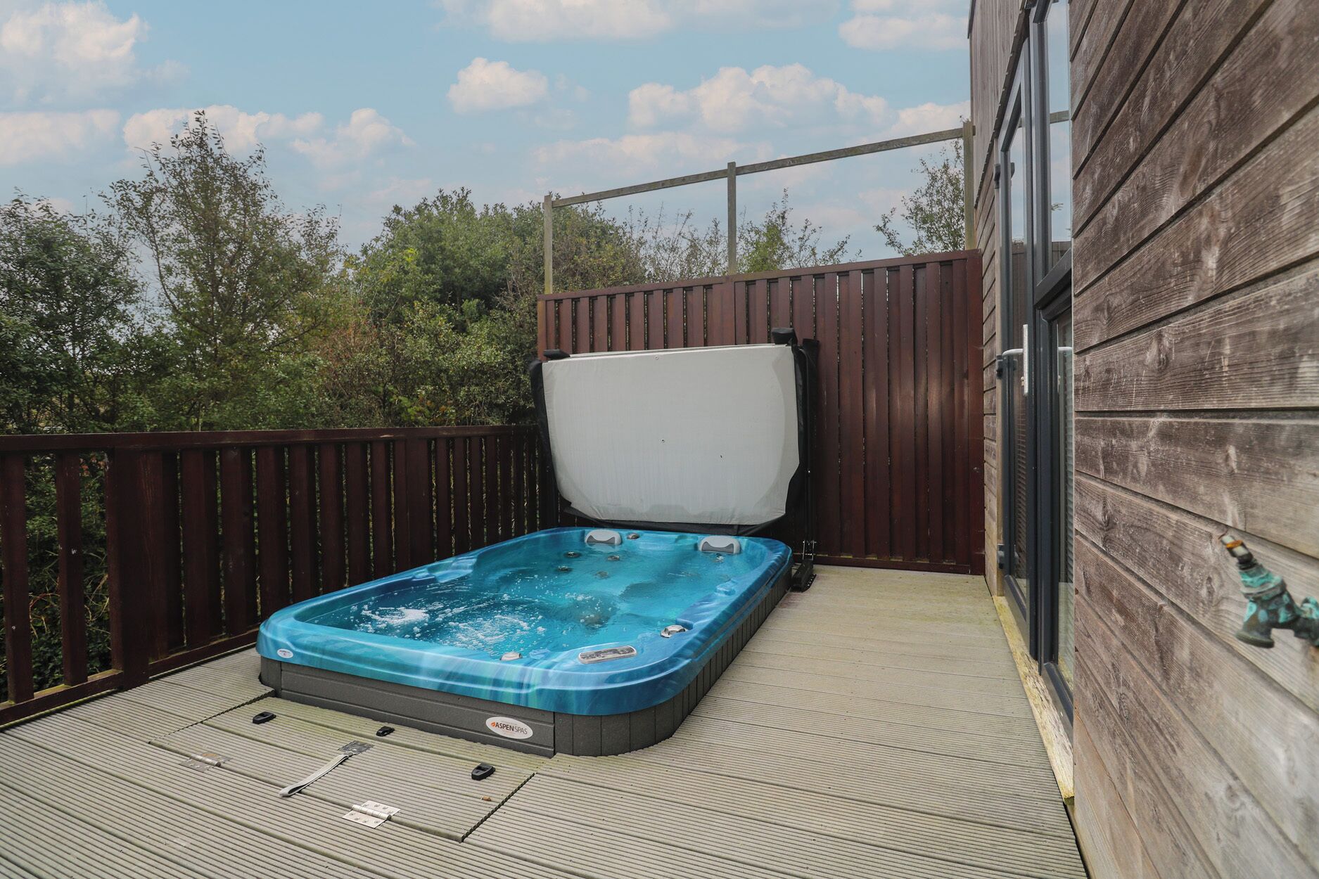 Un jacuzzi en una terraza de madera con una cerca de madera y un edificio al fondo.