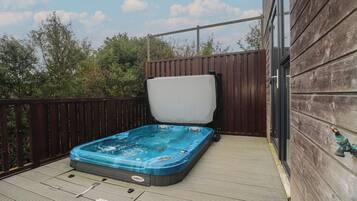 Un jacuzzi en una terraza de madera con una cerca de madera y un edificio al fondo.