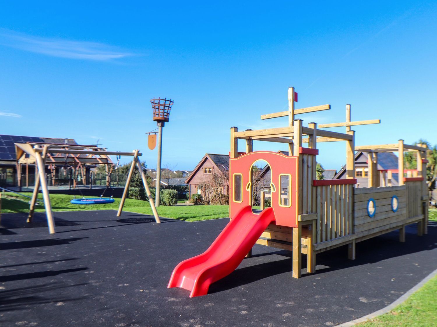 Un parque infantil con un tobogán rojo, estructuras para escalar y columpios.