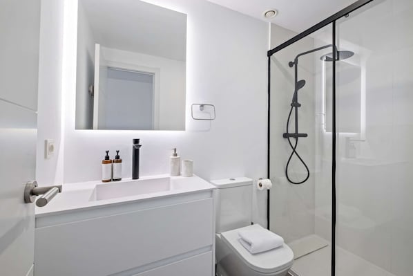 Et moderne badeværelse med en glasbrusekabine, en hvid vask med toiletartikler og et toilet.