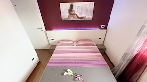 A bedroom with a bed, a bedside table, a nightstand, a painting on the wall, and a window with curtains.