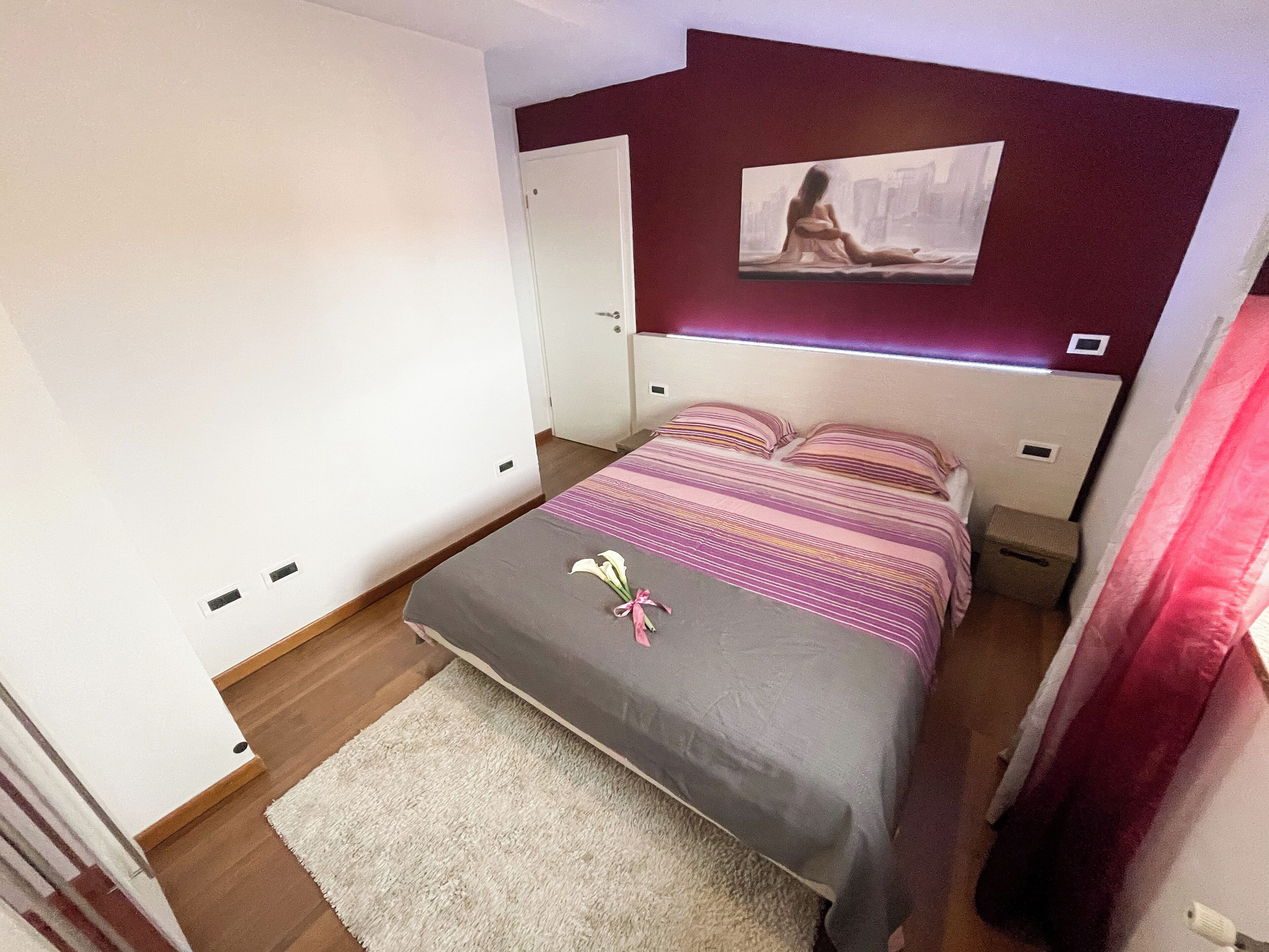 Une chambre à coucher avec un lit, une table de chevet, un tableau accroché au mur et une porte.