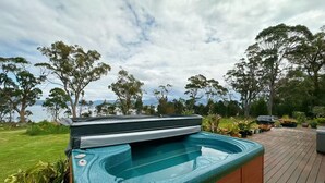 Un jacuzzi en una terraza de madera con vista a árboles y un cuerpo de agua.