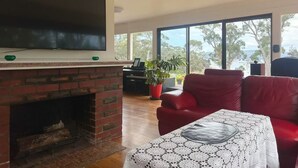 Una sala de estar con chimenea, televisor, un sofá rojo y ventanas amplias.