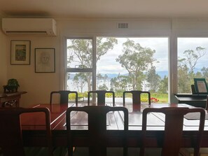 A dining area with a table and chairs, a piano, and a view of trees and mountains through large windows.