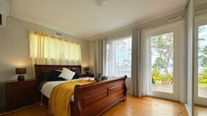 Un dormitorio con cama de madera, mesitas de noche, una ventana con cortinas y vistas al exterior.