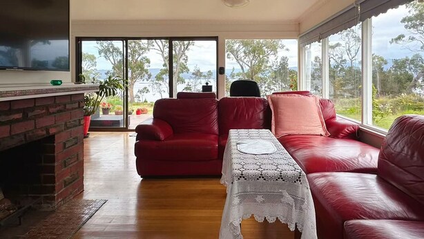 Una sala de estar con chimenea, sofás de cuero rojo, un televisor y ventanas amplias con vistas al exterior.