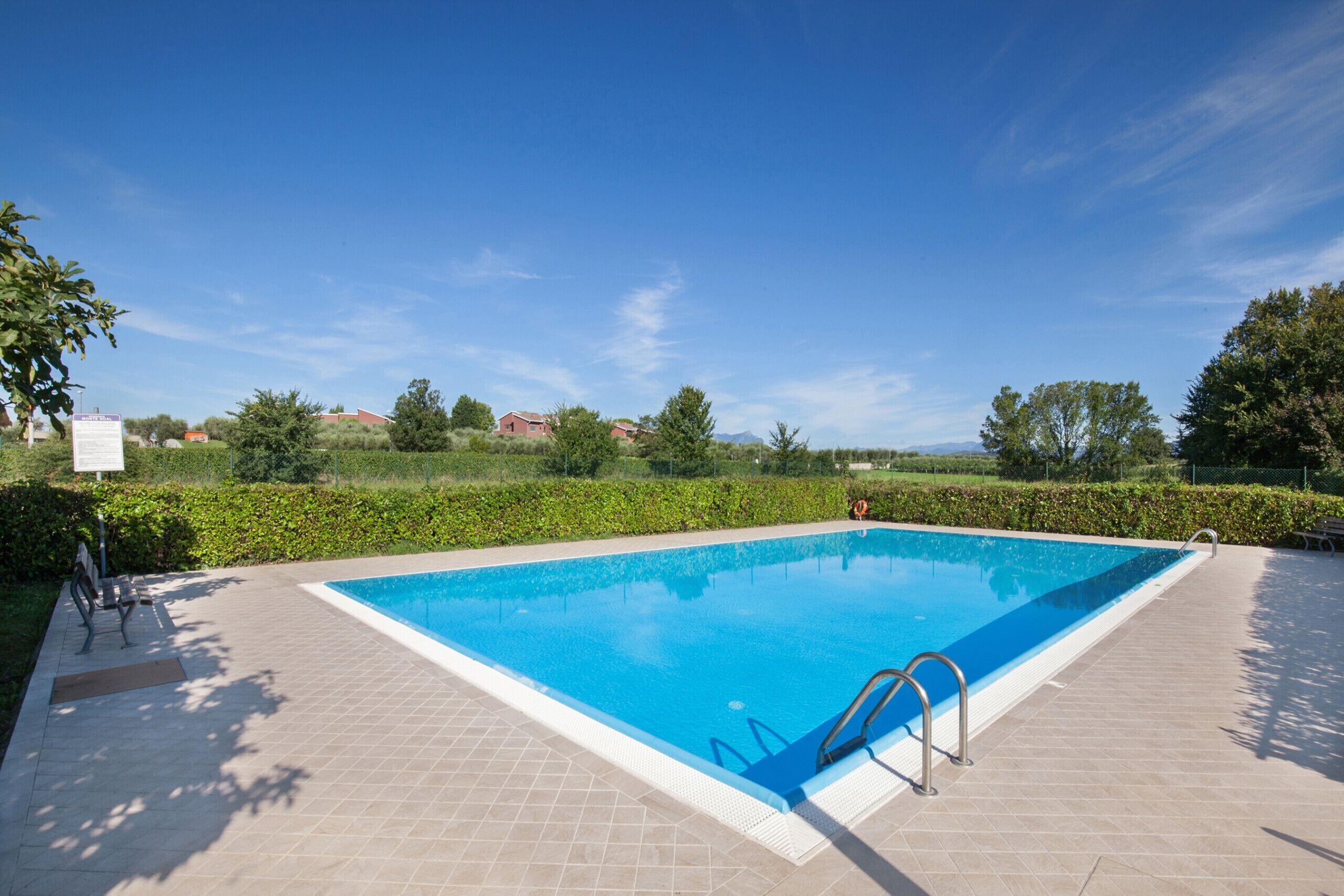 Una piscina rettangolare con bordo piastrellato, immersa nel verde sotto un cielo sereno.