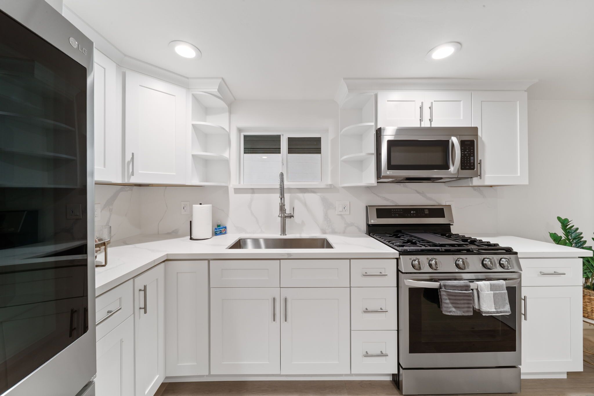 Una cocina moderna con armarios blancos, un lavamanos de acero inoxidable, un microondas, una estufa a gas y un horno empotrado.