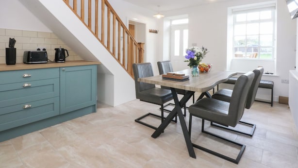 A modern kitchen with teal cabinets, a wooden staircase, and a dining area with a table and chairs.