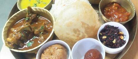 A traditional Indian meal with rice, curry, and chutney on a metal plate.