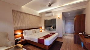 Una habitación de hotel con cama, mesitas de noche, escritorio, silla, armario y espejo.