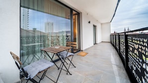 A balcony with a table and chairs, a glass door, and a view of a cityscape. - Garden side Emma accommodation in Monarh Tower (Timișoara)