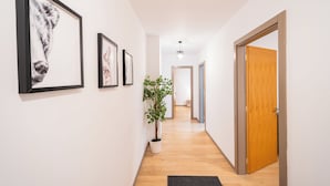 A hallway with framed artwork on the walls, a potted plant, and wooden flooring. - Garden side Emma accommodation in Monarh Tower (Timișoara)