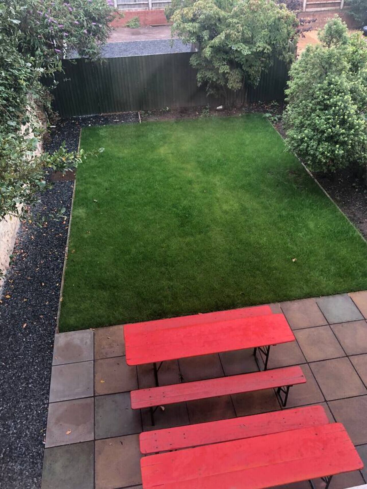 A backyard with a well-maintained lawn, a red picnic table, and a black fence.