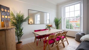 A dining area with a wooden table, red chairs, a mirror, and potted plants.