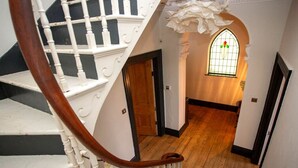 A staircase with white balusters and a wooden handrail leading to a room with a wooden floor and a stained glass window.