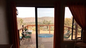 A bedroom with a large sliding glass door leading to an outdoor deck with a hot tub and chairs. - Romantic Yucca Valley Cabin with Hot Tub (Yucca Valley)