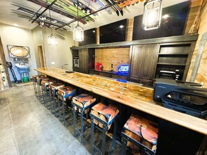 Uma área de bar com um balcão de madeira comprido, banquetas e uma impressora sobre o balcão.