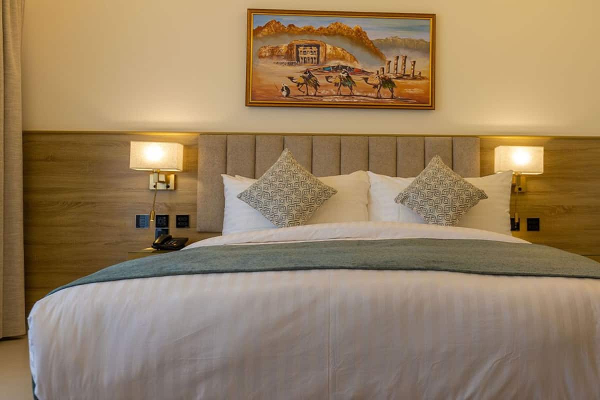 A hotel room with a large bed, two bedside lamps, patterned pillows, and a painting on the wall.