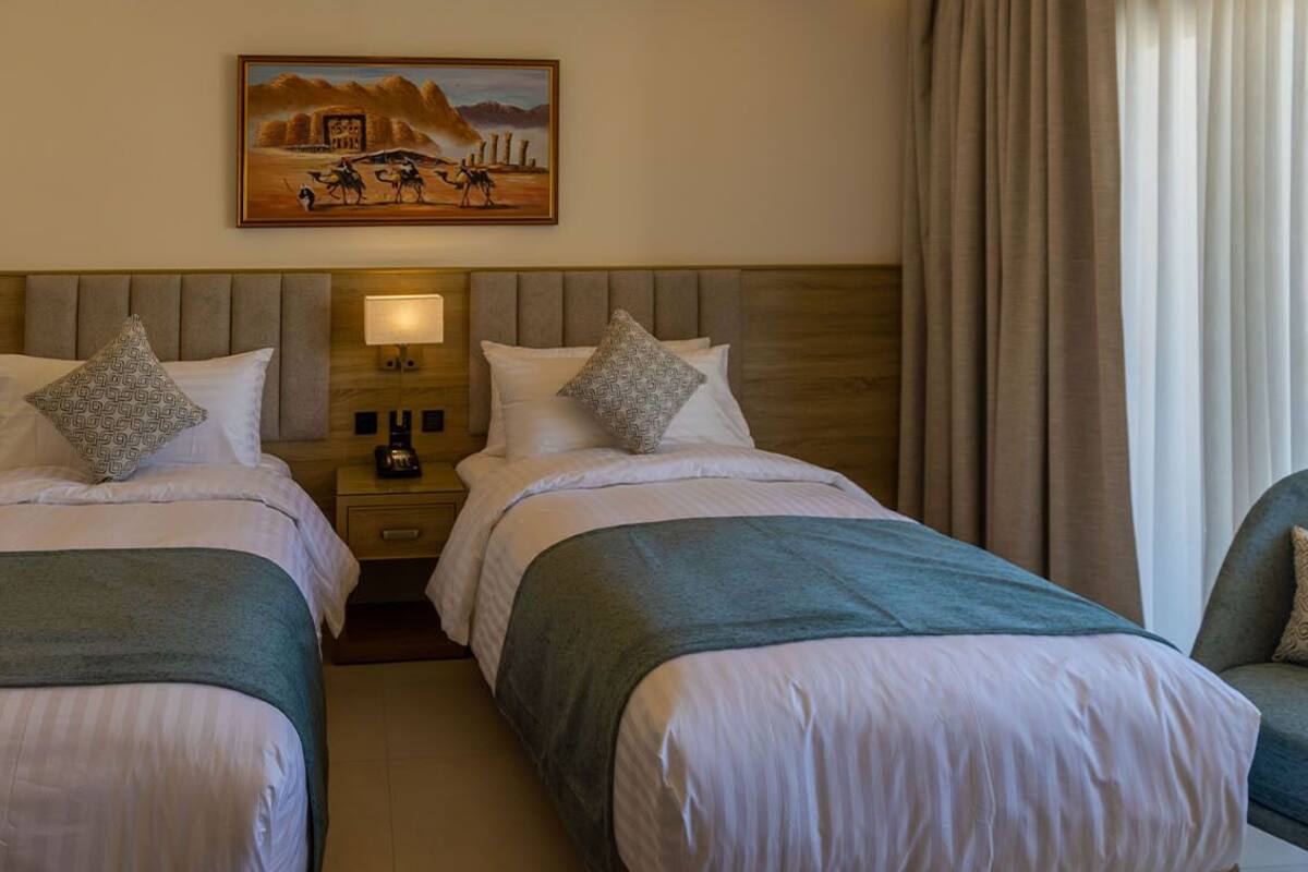 A hotel room with two single beds, a nightstand with a lamp, and a painting on the wall.
