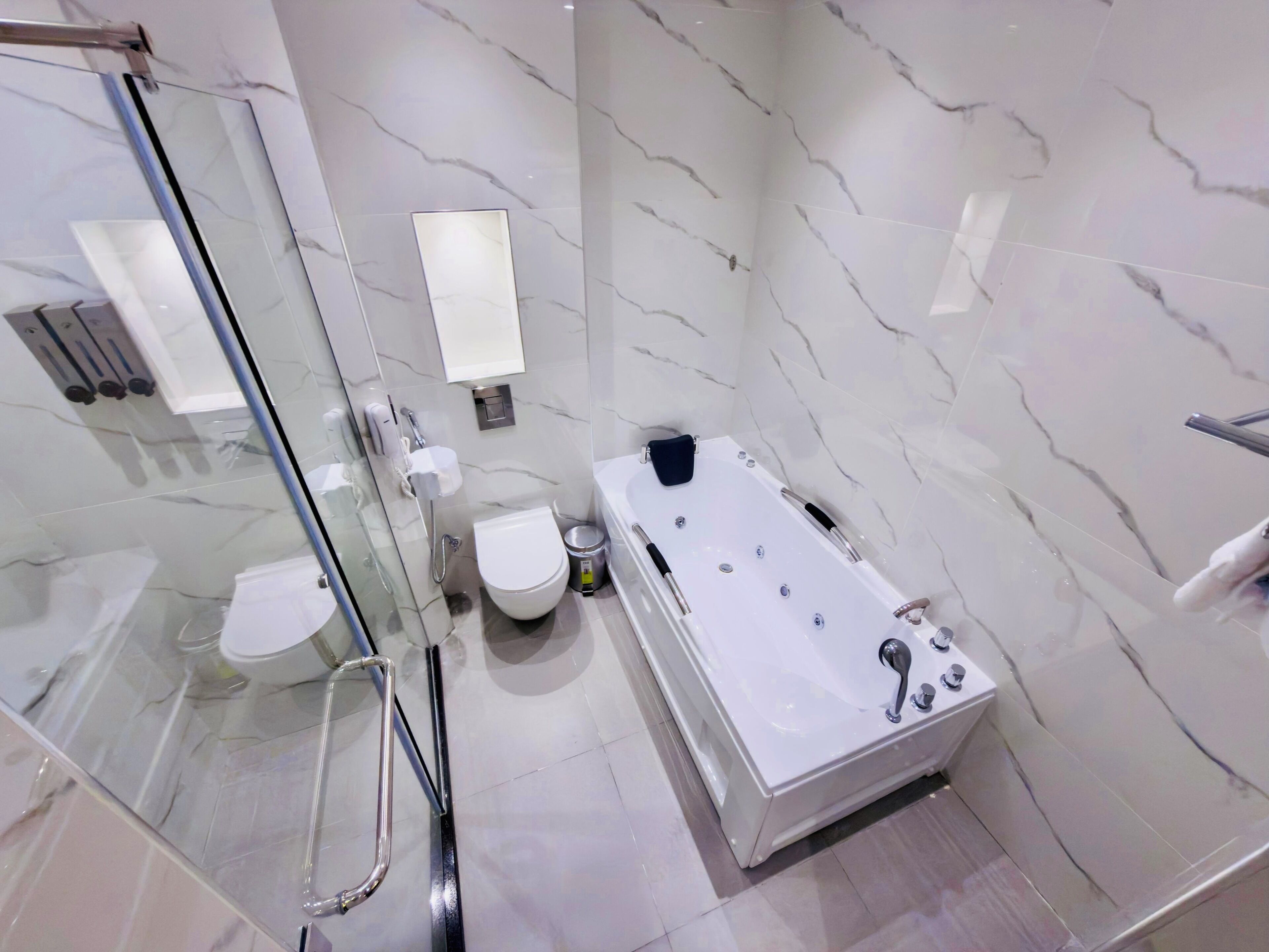 A modern bathroom with a glass shower enclosure, a toilet, a bathtub, and a hand dryer.