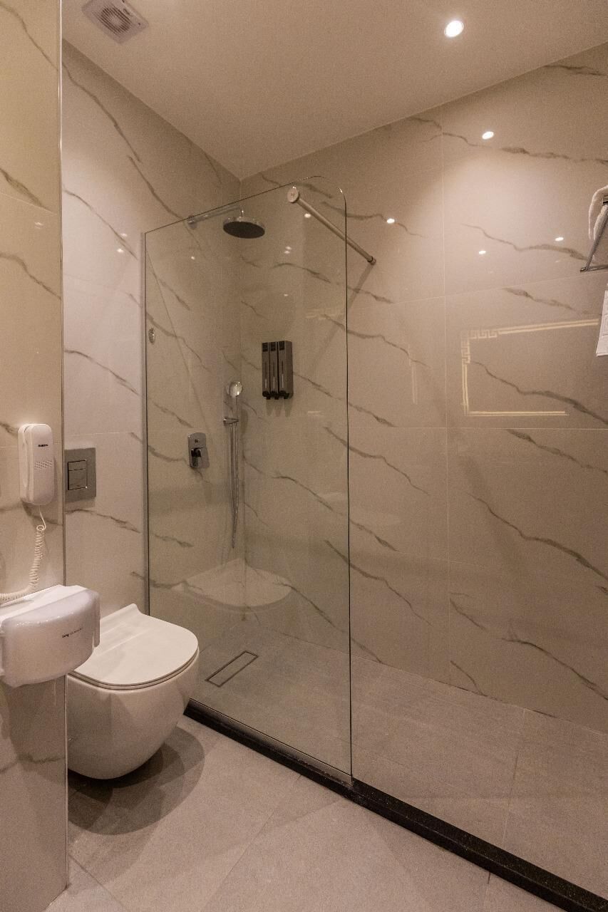 Une salle de bain moderne avec une douche à parois de verre, des toilettes et un mur en marbre.