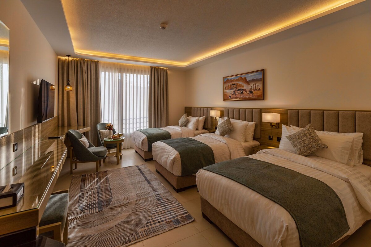 A hotel room with two beds, a desk, a chair, a TV, and a painting on the wall.