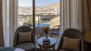 Ein Hotelzimmer mit Balkon, zwei Sesseln, einem kleinen Tisch mit einer Vase und einem Bett.