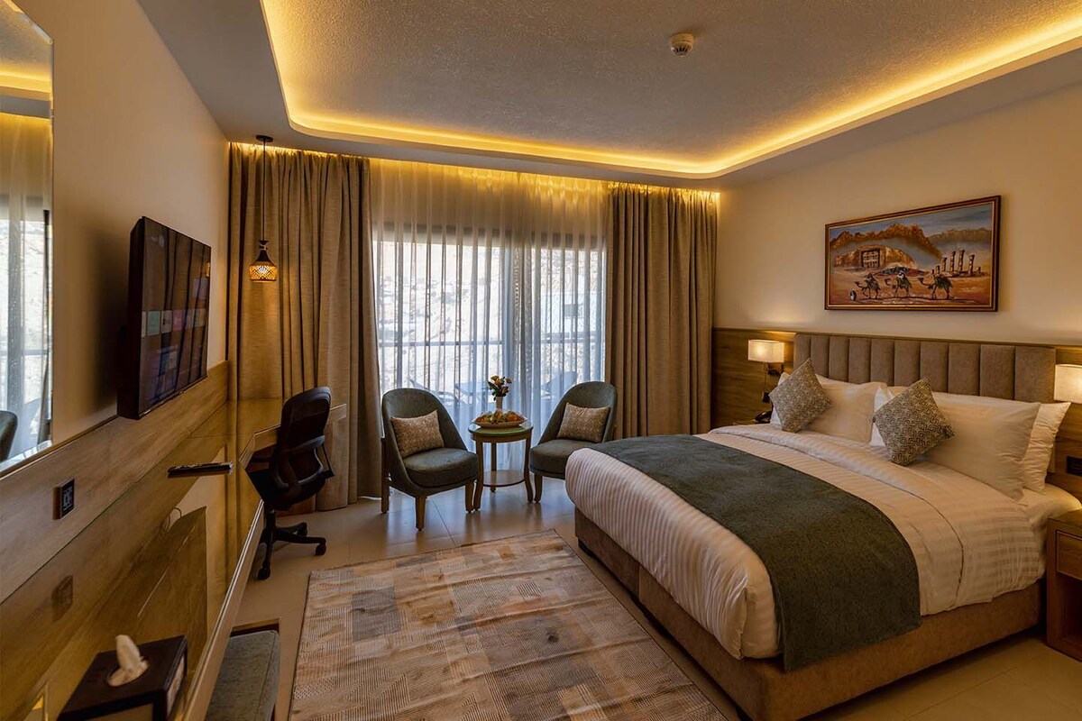 A hotel room with a large bed, two armchairs, a small table, a TV, and a painting on the wall.