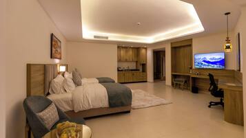 A modern hotel room with a bed, seating area, desk, and TV.