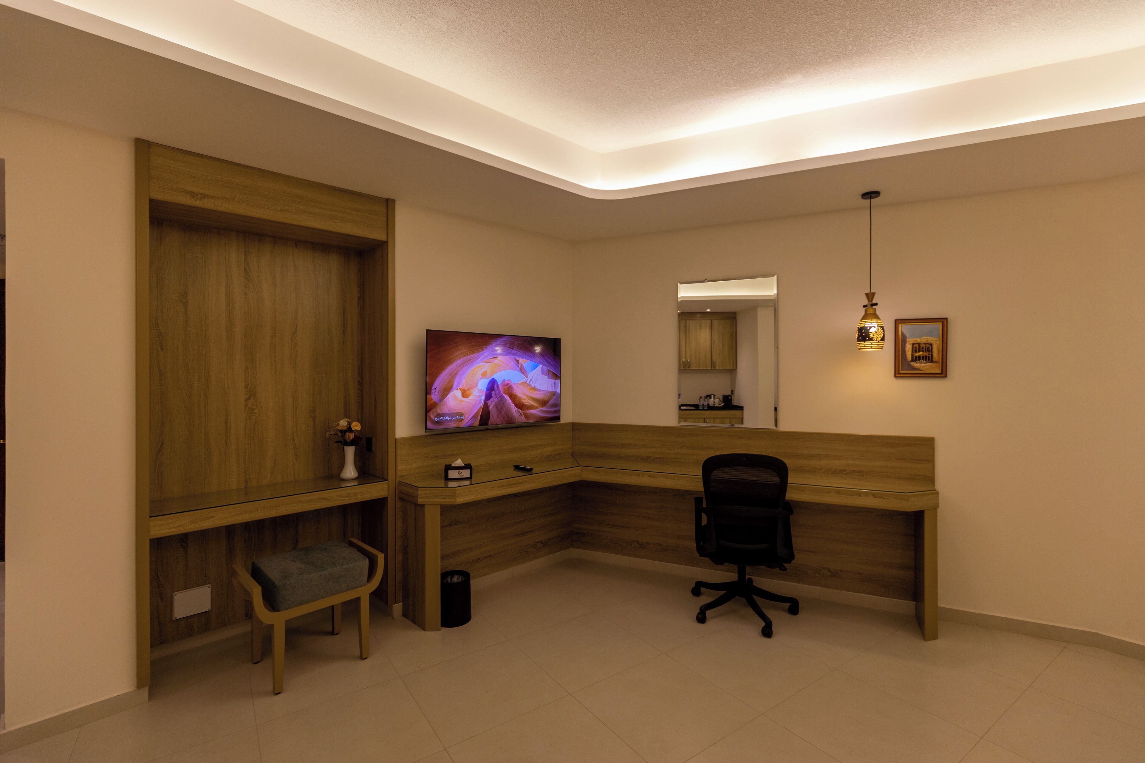 A modern office space with a wooden desk, a black office chair, a television, and a small bench.
