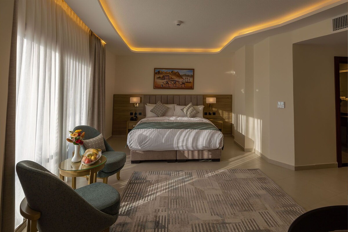 Ein modernes Hotelzimmer mit einem großen Bett, einer Sitzecke mit Sessel und Tisch und einem Bild an der Wand.