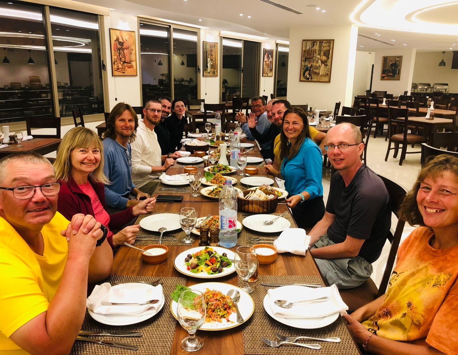 A group of people dining at a long table in a well-lit, modern dining area with artwork on the walls.