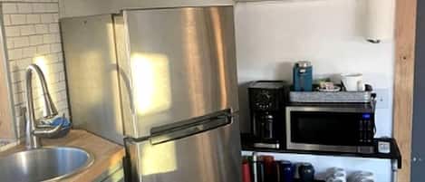 A compact kitchen with a stainless steel refrigerator, a sink, and a microwave.