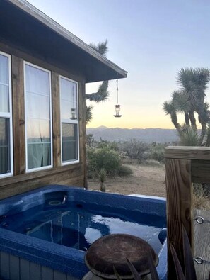 A wooden house with a hot tub, a window, and a view of mountains and palm trees.