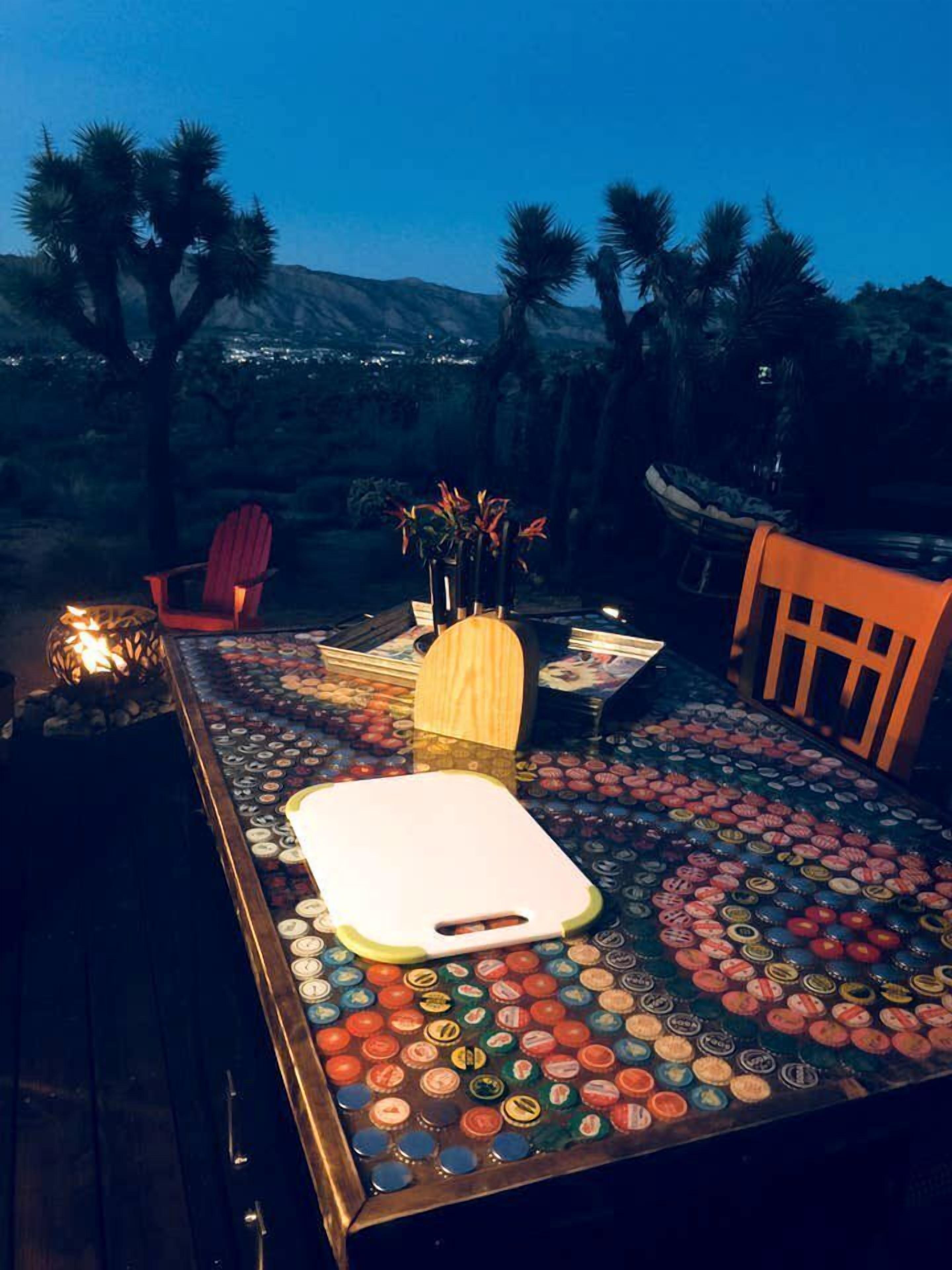 A dining table with a unique bottle cap mosaic design, surrounded by chairs and a vase with flowers.