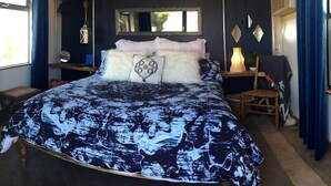 A bedroom with a bed, a bedside table, a chair, a mirror, and a window.
