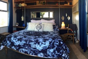 Une chambre à coucher avec un lit, une table de chevet, une chaise, un miroir et une fenêtre.