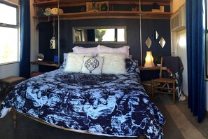 A bedroom with a bed, a bedside table, a chair, a mirror, and a window.