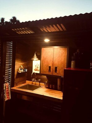 A small, rustic kitchen with wooden cabinets, a sink, and a hanging light fixture.