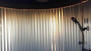 A bathroom with a shower, a ceiling-mounted light fixture, and a wall with vertical metal slats.
